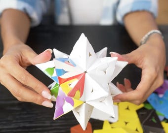 May include: A geometric star-shaped puzzle constructed from multiple triangular pieces. The exterior surfaces are primarily white, while the interior facets reveal a vibrant spectrum of colours including red, yellow, blue, green, and purple.