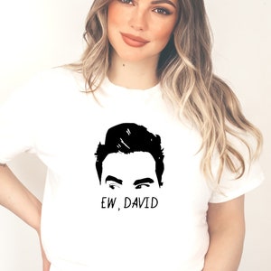 May include: White t-shirt with a black graphic of a person's eyes and hair, with the text "EW, DAVID" below the graphic. The t-shirt is made of a soft material.