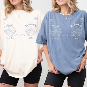 Puede incluir: Dos camisetas, una marfil y otra azul, con un diseño de conchas marinas y el texto "Olivia's Bachelorette Punta Cana 2026". Las camisetas tienen mangas cortas y un corte holgado, ideales para una despedida de soltera.