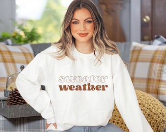 May include: White sweatshirt with the text "sweater weather" in brown lettering. The text is in a retro font style.