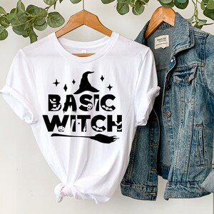 May include: White t-shirt with a black graphic of a witch's hat, bats, and the text "BASIC WITCH".