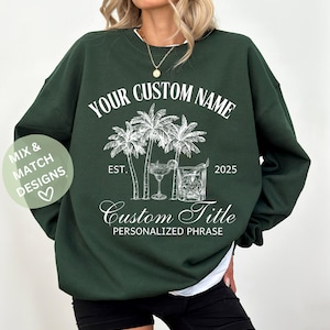 May include: Dark green sweatshirt featuring white text and illustrations. The design includes palm trees, cocktail glasses, and the words "YOUR CUSTOM NAME", "Custom Title", and "PERSONALIZED PHRASE". The sweatshirt has a white collar.
