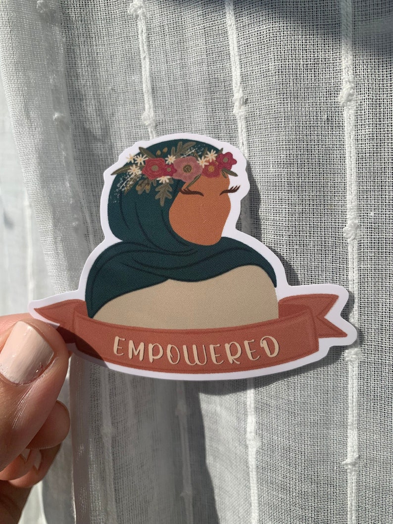 Pu&ograve; includere: Un adesivo con una donna che indossa un velo turchese e una corona di fiori. La donna guarda di lato e l'adesivo ha la parola "EMPOWERED" scritta su uno stendardo rosso.