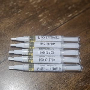 May include: Six clear tubes with white caps and labels. The labels list different scents, including Black Chamomile, Pink Chiffon, London Mist, Jasmine + Labdanum.