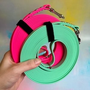 May include: Two dog leashes, one pink and one green, are rolled up together. The leashes are made of a thick, durable material and have a black strap.