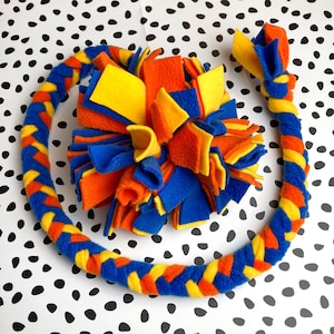 May include: A colorful dog toy set featuring a braided ring and a fluffy ball, both made of blue, orange, and yellow fleece. The ring is approximately 12 inches in diameter. The toys are designed for interactive play and enrichment.
