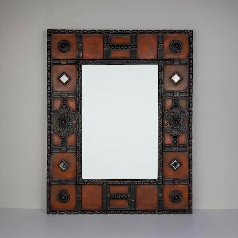 Pu&ograve; includere: Specchio rettangolare con cornice decorativa. La cornice presenta un motivo ripetuto di quadrati e cerchi nelle tonalit&agrave; del marrone e del nero. Piccoli accenti a forma di diamante e specchio quadrato sono incorporati nel design.