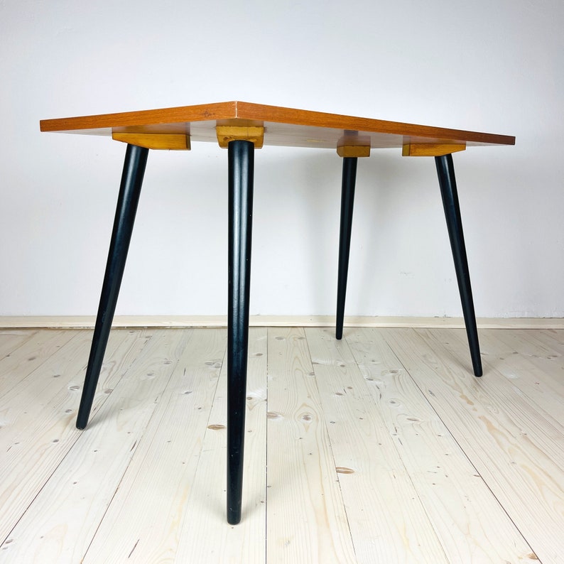 Peut inclure: Une table rectangulaire en bois avec un plateau brun clair et des pieds noirs. La table a un design simple et est faite de bois massif.