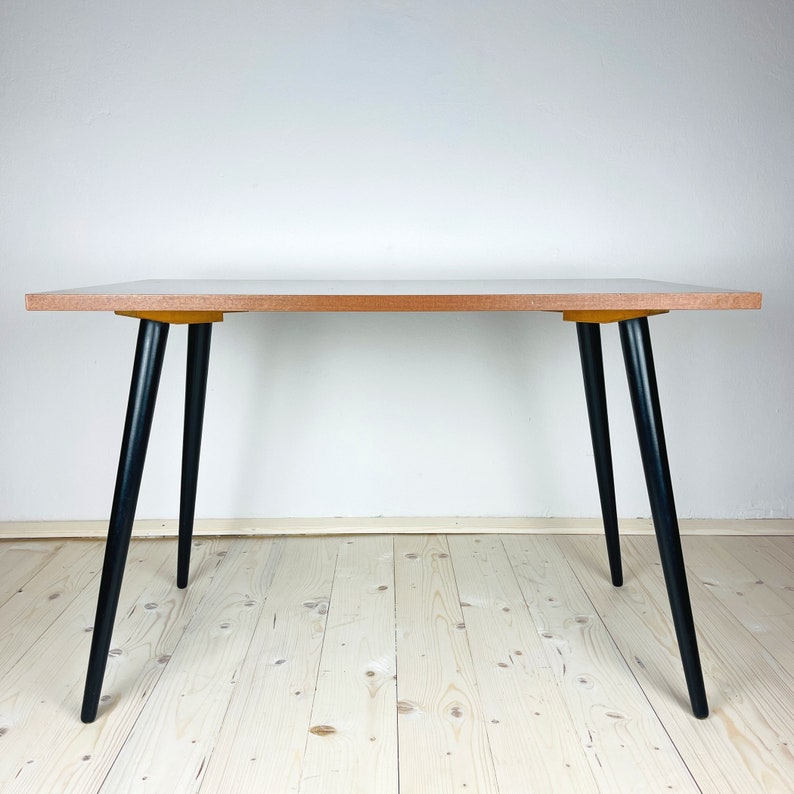 Peut inclure: Une table en bois simple avec un plateau en bois clair et des pieds noirs. La table est sur un plancher en bois clair.