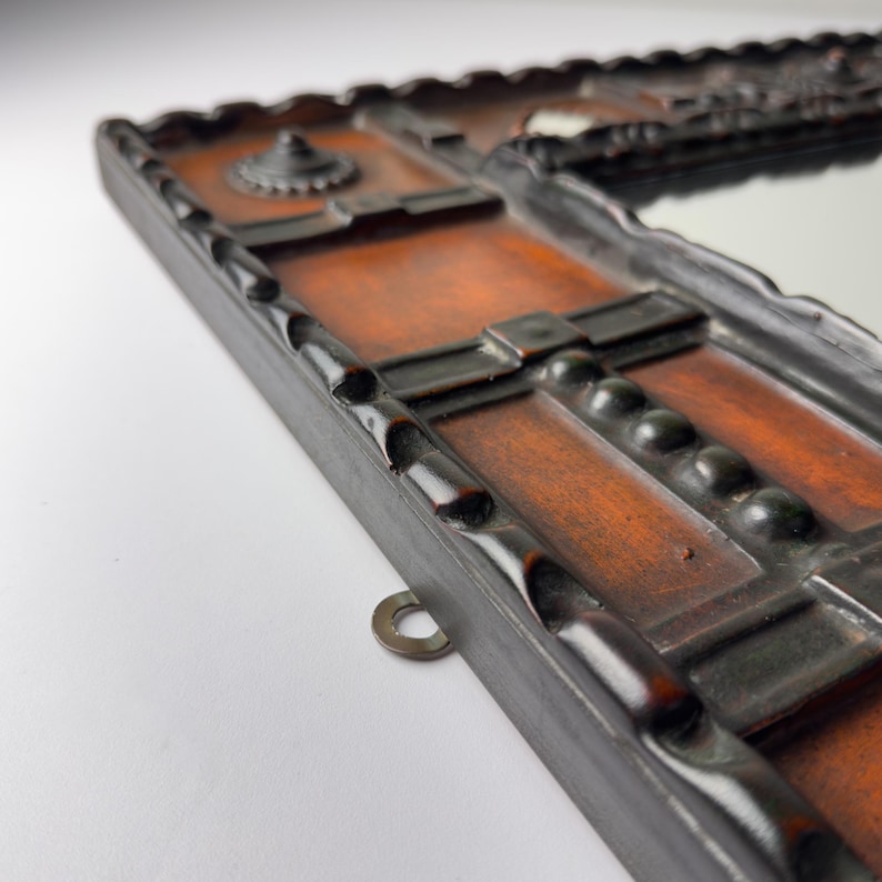 Pu&ograve; includere: Primo piano di una cornice rettangolare in legno per specchio con finitura marrone scuro. La cornice presenta un design decorativo intagliato con uno specchio centrale. Un anello di metallo &egrave; attaccato alla cornice per appenderla. La cornice ha un motivo geometrico dettagliato.