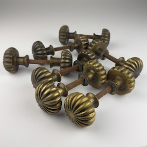 May include: A collection of antique brass door knobs. Each knob has a ribbed, rounded design and is attached to a metal rod. The knobs have a warm, aged patina, suggesting vintage or reclaimed hardware. Ideal for home renovation projects.