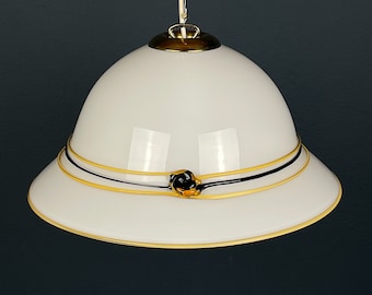 May include: A white glass pendant light fixture shaped like a safari hat with a black and gold trim and a black flower accent.