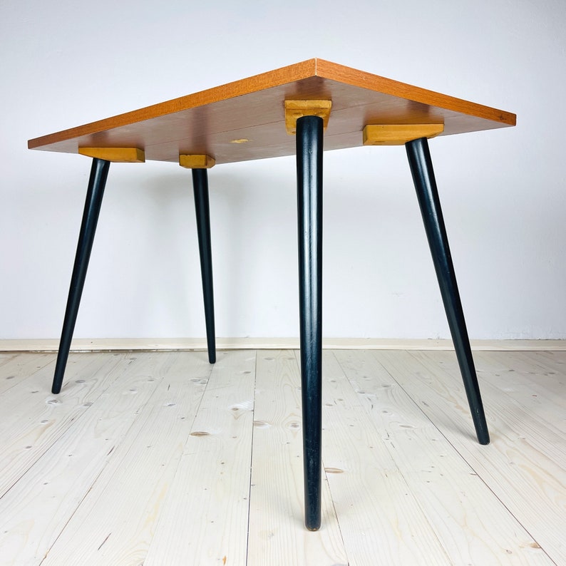 Peut inclure: Une table de style moderne du milieu du si&egrave;cle avec un plateau en bois clair et des pieds noirs. La table a un design simple et est parfaite pour un petit espace.