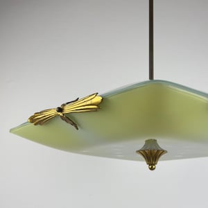Puede incluir: Una lámpara colgante cuadrada de estilo vintage con una pantalla de cristal verde pálido. La lámpara presenta un acento de libélula dorada y una pieza final decorativa dorada. La luz cuelga de una varilla marrón oscuro.