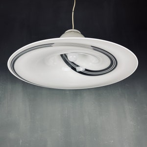 May include: A white ceiling light fitting with a swirling black and white design. The light fitting is suspended from the ceiling by a white cord.