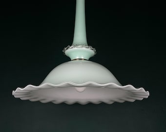 May include: A light green glass pendant light with a scalloped white glass shade. The light has a gold metal top and a decorative band around the center of the stem.