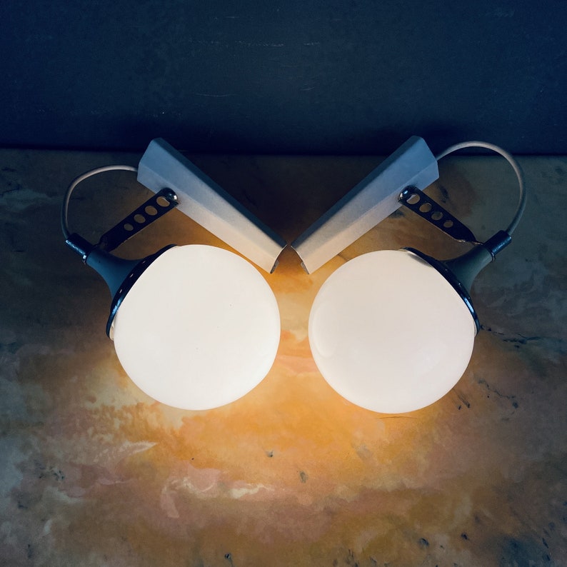 Pode incluir: Duas luzes brancas em forma de globo com detalhes cromados e uma base de metal cinza. As luzes est&atilde;o montadas em uma parede.
