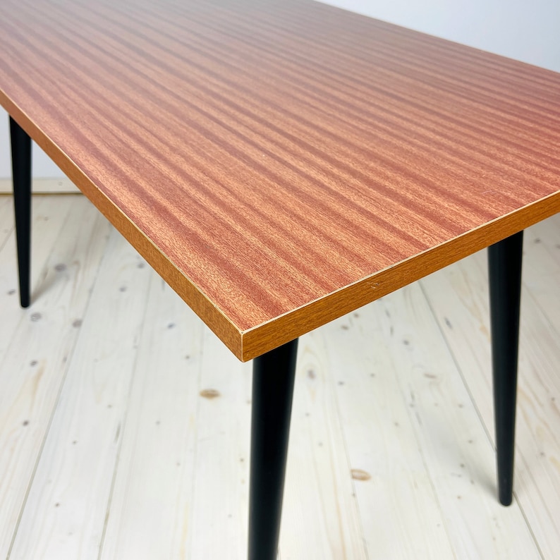 Peut inclure: Une table rectangulaire avec un plateau en stratifi&eacute; bois brun et des pieds noirs. La table a un design simple et moderne du milieu du si&egrave;cle.