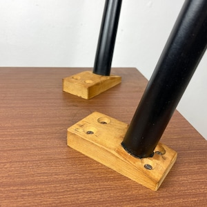 Peut inclure: Gros plan sur deux pieds en m&eacute;tal noir fix&eacute;s &agrave; une base de table en bois. Les pieds sont fix&eacute;s &agrave; la base &agrave; l'aide de vis et ont une finition noire. La base est en bois brun clair et a une surface lisse.