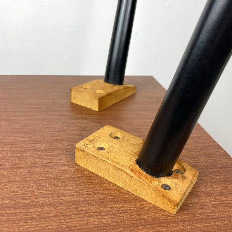 Peut inclure: Gros plan sur deux pieds en m&eacute;tal noir fix&eacute;s &agrave; une base de table en bois. Les pieds sont fix&eacute;s &agrave; la base &agrave; l'aide de vis et ont une finition noire. La base est en bois brun clair et a une surface lisse.