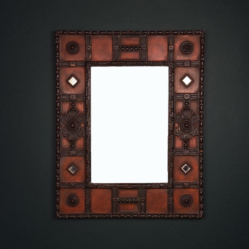 Pu&ograve; includere: Specchio decorativo rettangolare con cornice color rame. La cornice presenta motivi geometrici, accenti floreali e piccoli inserti a specchio. Lo specchio &egrave; progettato per essere appeso a una parete.