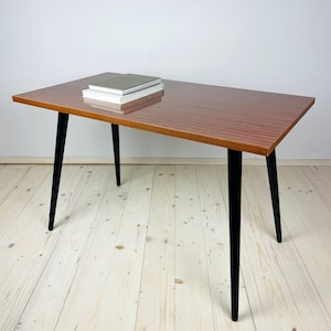 Peut inclure: Une table basse rectangulaire avec un plateau en bois brun et des pieds noirs. La table a un design &eacute;l&eacute;gant et moderne et est parfaite pour un salon ou un bureau.