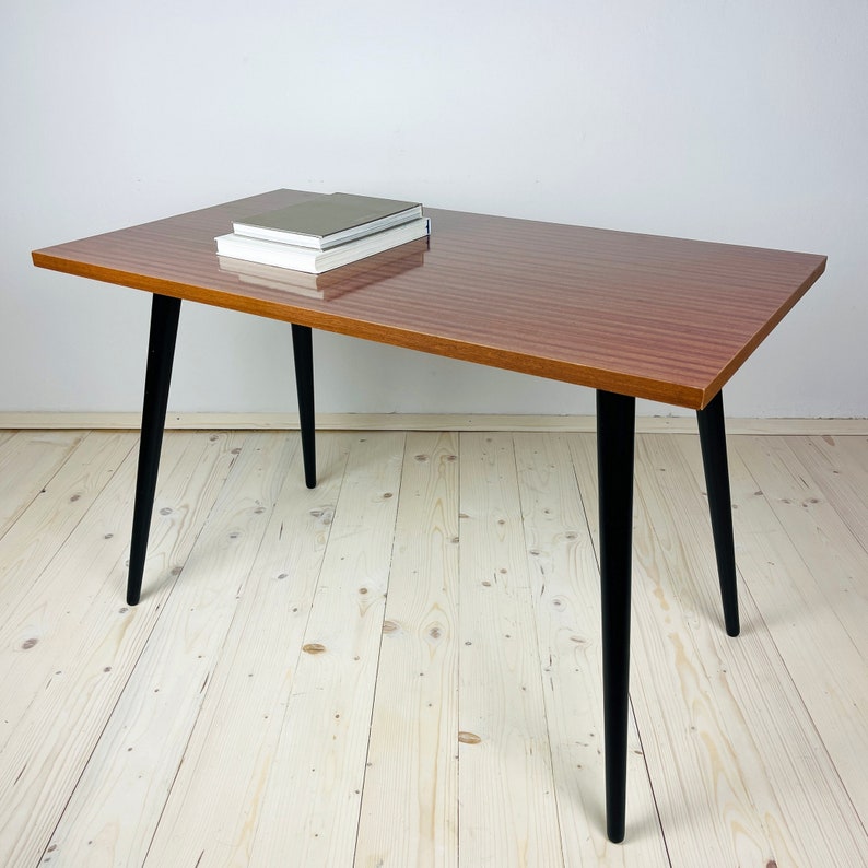 Peut inclure: Une table basse rectangulaire avec un plateau en bois brun et des pieds noirs. La table a un design &eacute;l&eacute;gant et moderne et est parfaite pour un salon ou un bureau.