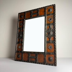 Pu&ograve; includere: Specchio rettangolare ornato con una cornice decorativa. La cornice presenta pannelli color rame e dettagli in metallo scuro. Disegni floreali e geometrici adornano la cornice, aggiungendo un fascino vintage. Un elemento decorativo per la casa.