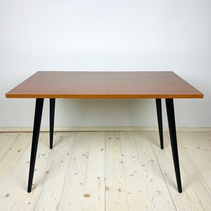 Peut inclure: Une table rectangulaire en bois avec un plateau en bois brun et des pieds noirs. La table a un design simple et est parfaite pour un petit espace.