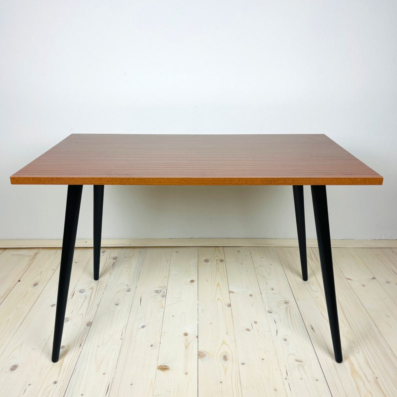 Peut inclure: Une table rectangulaire en bois avec un plateau en bois brun et des pieds noirs. La table a un design simple et est parfaite pour un petit espace.
