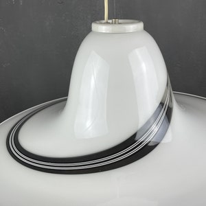 May include: White glass pendant light with black and white stripes. The light has a curved, modern design.