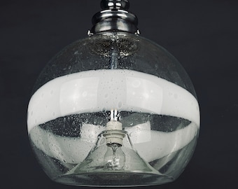 May include: A clear glass globe pendant light with a white band around the middle. The light has a silver metal top and a single light bulb inside.