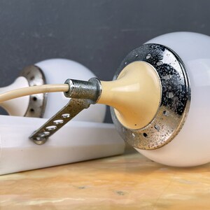 Pode incluir: Duas l&acirc;mpadas brancas em forma de globo com um interior creme e uma base de metal prateado. As l&acirc;mpadas t&ecirc;m um padr&atilde;o decorativo de pequenos furos ao redor da base.