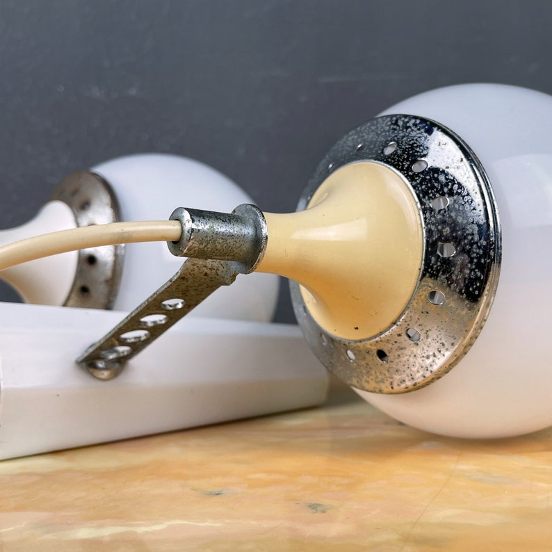 Pode incluir: Duas l&acirc;mpadas brancas em forma de globo com um interior creme e uma base de metal prateado. As l&acirc;mpadas t&ecirc;m um padr&atilde;o decorativo de pequenos furos ao redor da base.