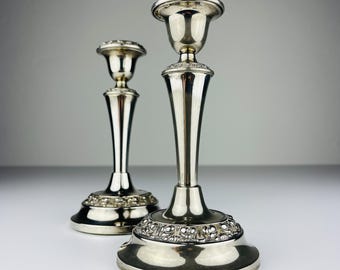 May include: A pair of silver candlestick holders with ornate designs. The holders have a tall, slender base and a cup-shaped top. The base is decorated with a floral pattern. The holders are made of silver and have a polished finish.
