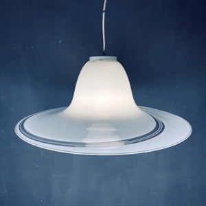 May include: A white glass pendant light with a wide, circular, saucer-shaped base and a bell-shaped top. The base has a thin, silver-coloured band around the edge.