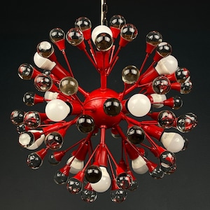 Op de afbeelding: Een rode Sputnik-stijl kroonluchter met meerdere armen die zich uitstrekken vanuit een centrale bol. De armen bevatten heldere, witte en donkergekleurde glazen bollen en gloeilampen, waardoor een unieke lamp ontstaat.