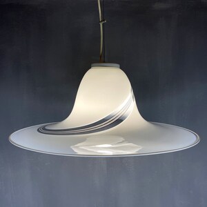 May include: A white pendant light with a wide, curved, saucer-shaped shade. The shade has a silver and black swirl design.