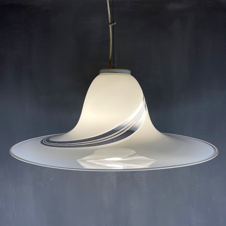 May include: A white pendant light with a wide, curved, saucer-shaped shade. The shade has a silver and black swirl design.