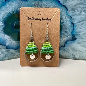 May include: A pair of green and silver teardrop-shaped earrings with a silver bead charm. The earrings are on a brown card with the text "Our Journey Jewelry".
