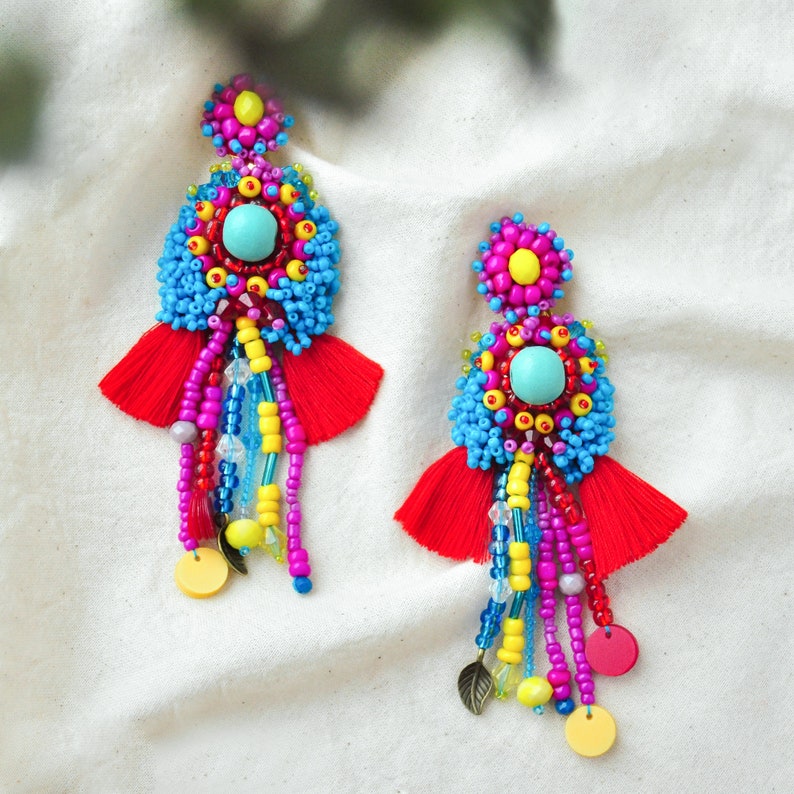 May include: A pair of colorful beaded earrings with red tassels. The earrings feature blue, yellow, pink, and turquoise beads, and a turquoise stone in the center of each earring.