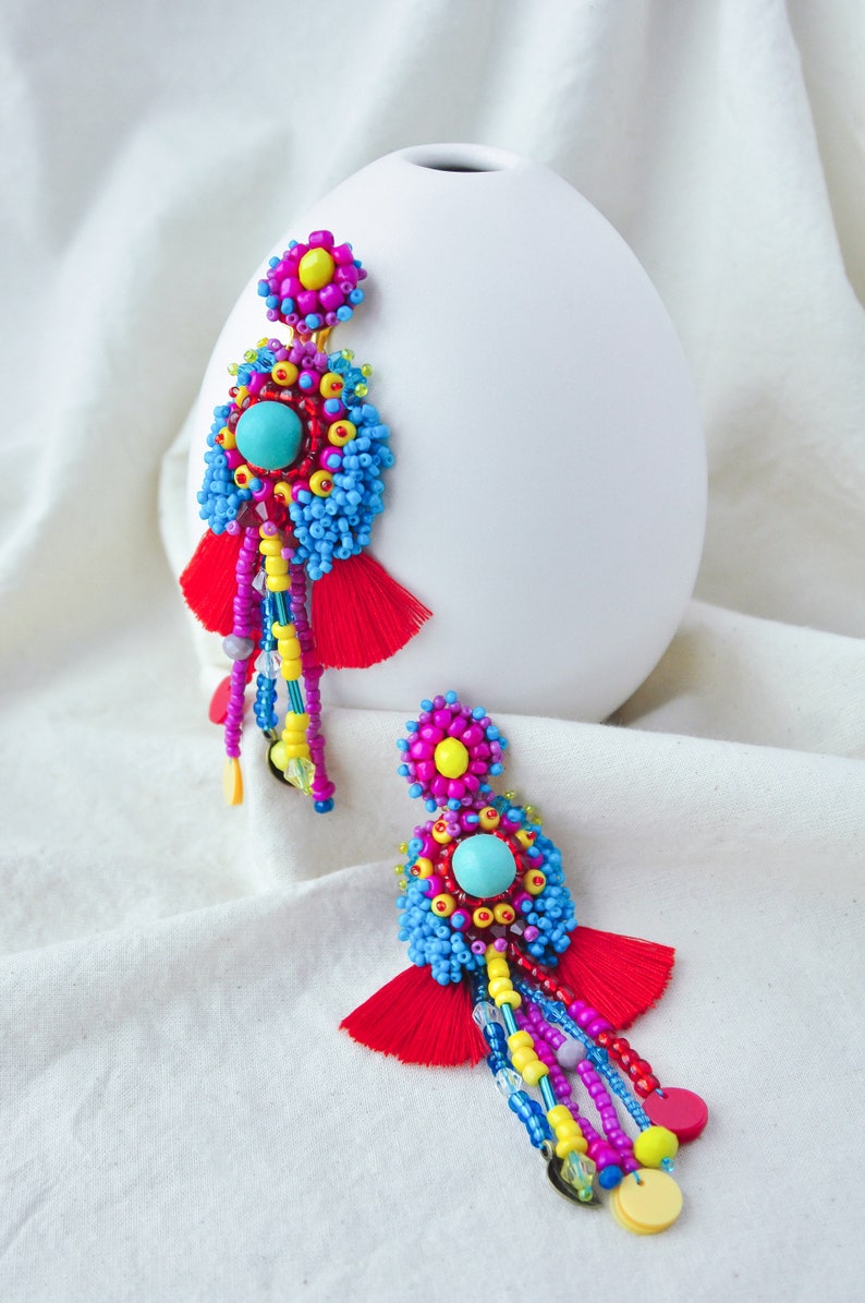 May include: A pair of colorful beaded earrings with red tassels. The earrings feature a turquoise bead in the center of each flower-shaped design.