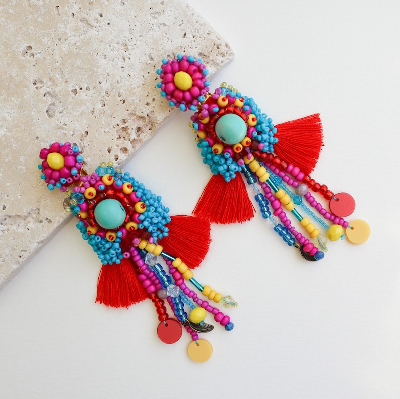May include: A pair of colorful beaded earrings with turquoise accents and red tassels. The earrings are made with a variety of beads, including blue, yellow, pink, and red.