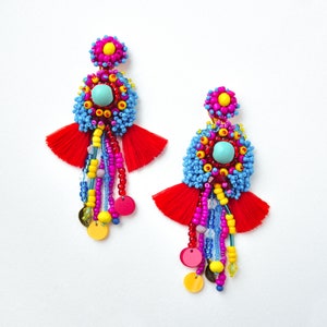 May include: A pair of colorful beaded earrings with red tassels, blue and yellow beads, and a turquoise stone in the center.