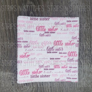 May include: White fabric with a pink and purple repeating pattern of the words "little sister".