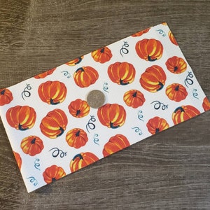 May include: White fabric with a repeating pattern of orange pumpkins with yellow highlights and green stems. The pumpkins vary in size and are interspersed with blue swirls. A quarter is on the fabric for scale.