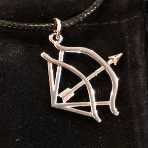 May include: A silver necklace with a bow and arrow pendant. The pendant is a simple design with a thin bow and arrow.