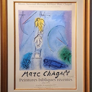 Pode incluir: Impressão artística emoldurada de um cartaz de exposição de Marc Chagall. A obra de arte apresenta uma paleta de cores azul e amarelo com figuras subindo uma escada. O texto inclui o nome do artista e detalhes da exposição.