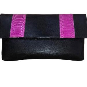 May include: Black leather clutch with a flap closure. The clutch features two vertical magenta snakeskin stripes. The bag is rectangular and appears to be made of a smooth leather material.