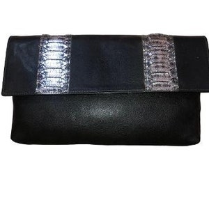 May include: Black leather clutch with a flap closure. The clutch features a silver and gray snakeskin pattern across the center. The bag is rectangular and appears to be made of genuine leather.